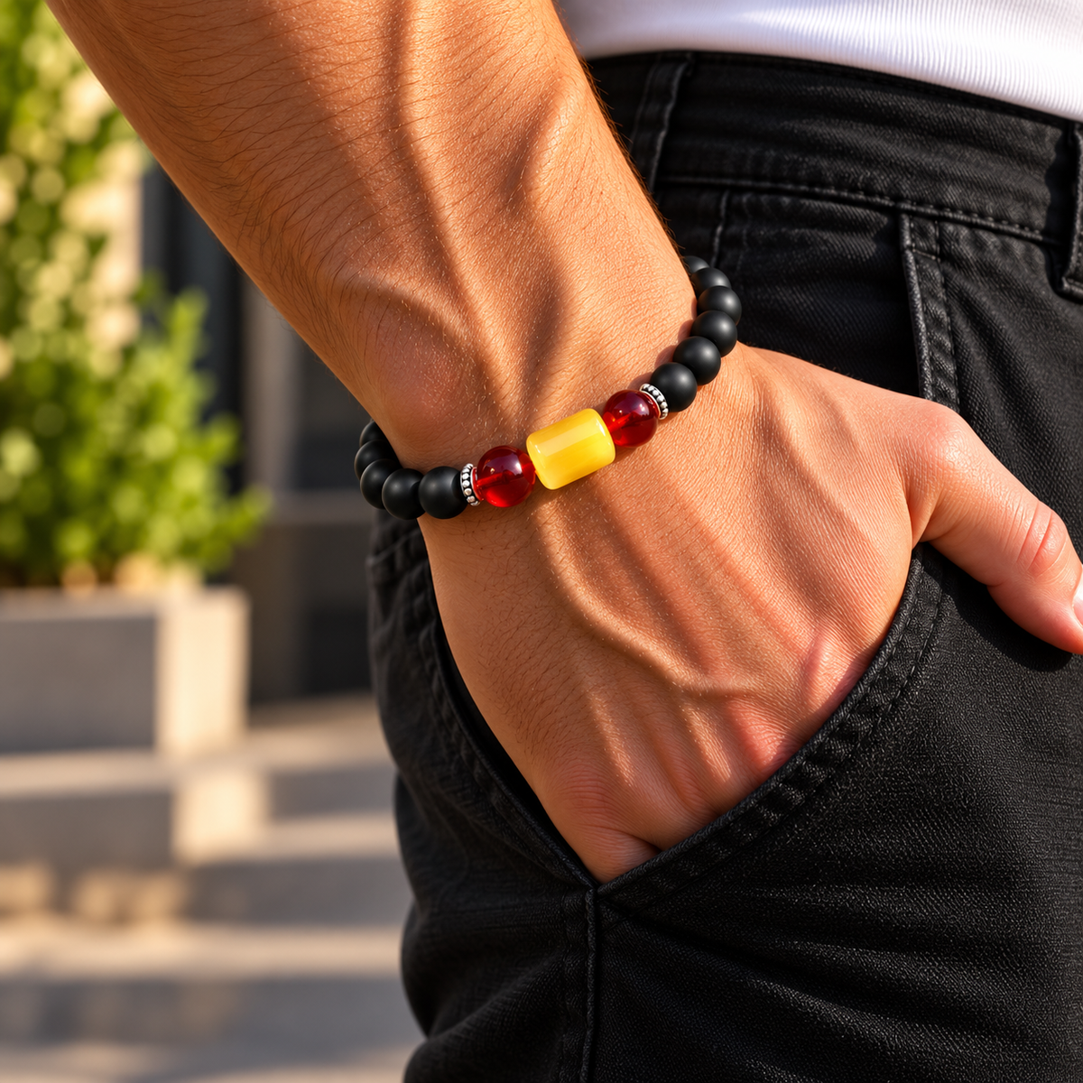 Mann trägt ein rot-gelbes Bernstein Armband mit schwarzen Onyx-Perlen und Ringen aus 925 Silber am Handgelenk.